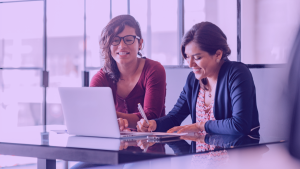 A foto mostra duas mulheres durante uma reunião. simbolizando o momento no qual o head de produto avalia um product manager na rotina de trabalho
